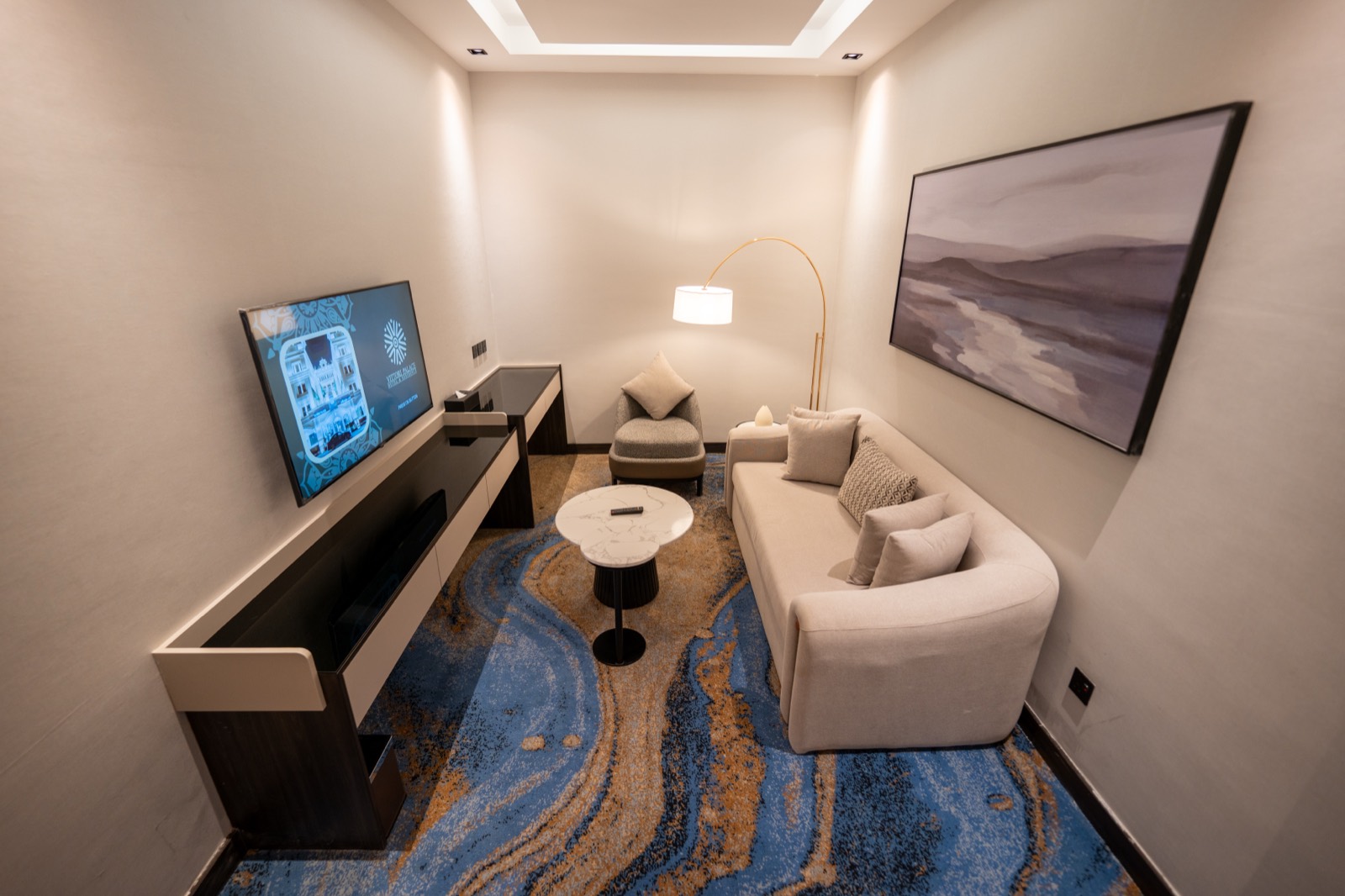 Deluxe Room with a curved sofa, writing desk and patterned carpet